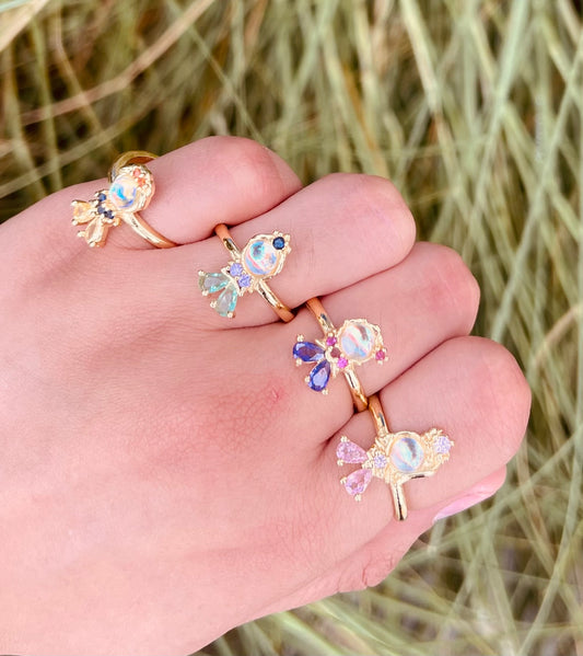 Anillos de fantasía con piedra central iridiscente y gemas de colores